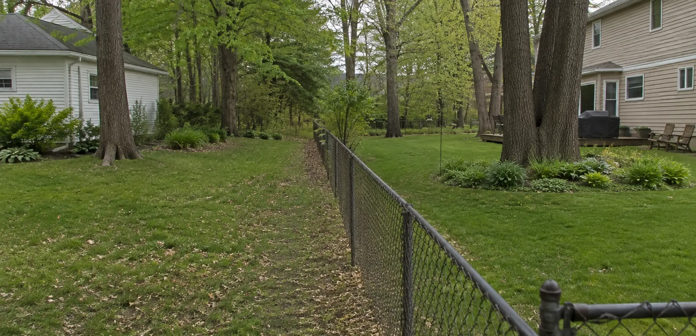 Rear yard of a Washtenaw County home showing a wooden privacy fence and property stakes along the lot line