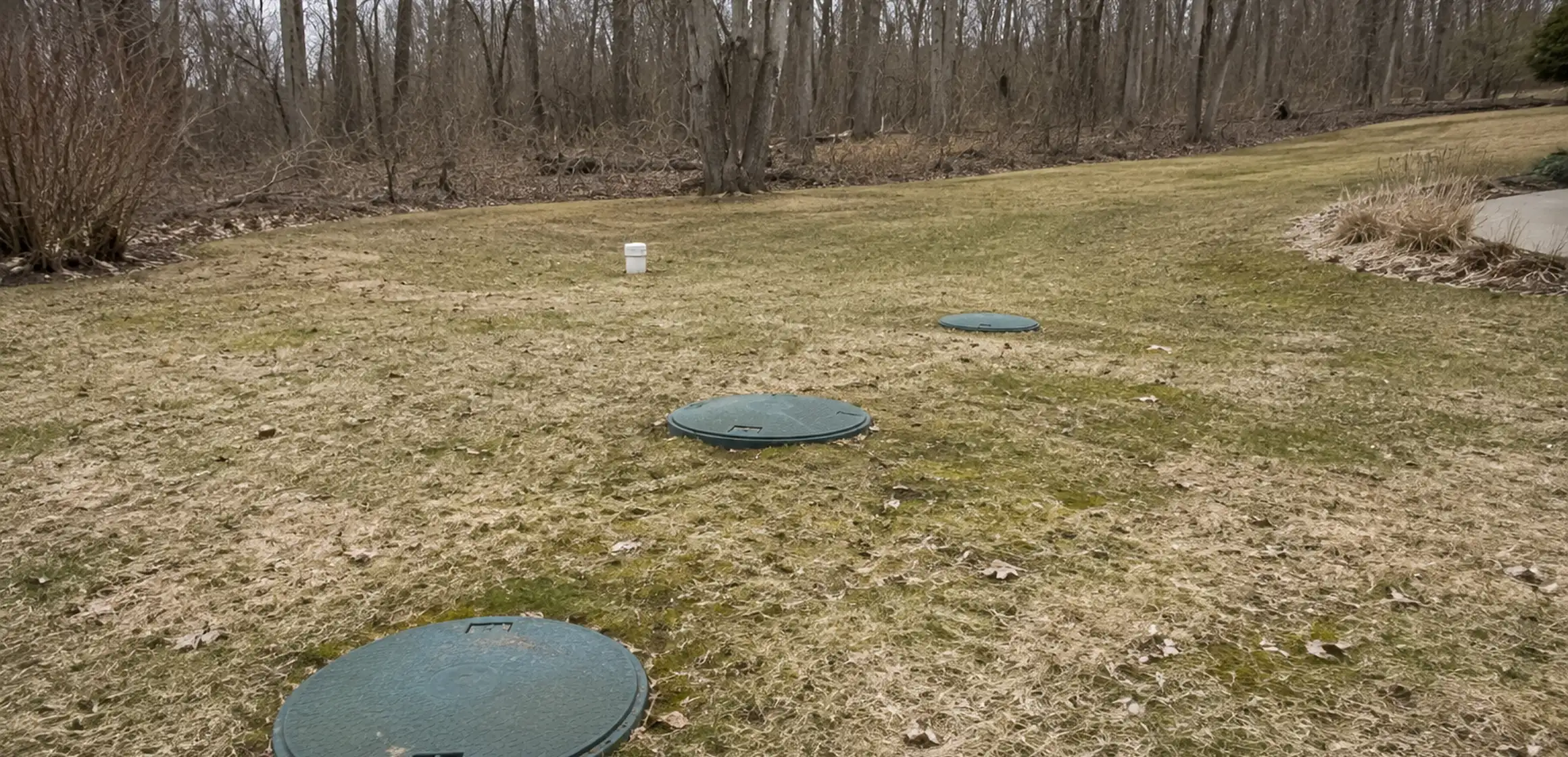 House with a septic tank access cover and raised bed drain field in a rural yard